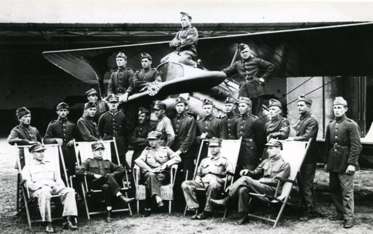 Longin Grudzień w grupie na tle hangaru i samolotu.