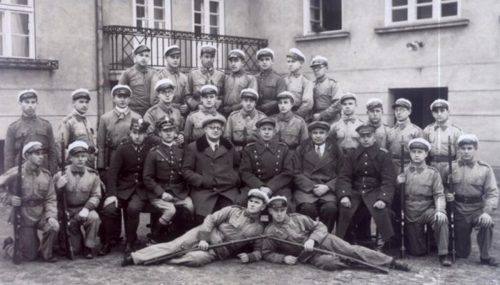 Oddział umundurowanych uczni&oacute;w przysposobienia wojskowego (Hufiec Szkolny) wraz z nauczycielami (po cywilnemu) na dziedzińcu szkoły mleczarskiej we Wrześni. Wśr&oacute;d nauczycieli Hugon Jan Katzer.